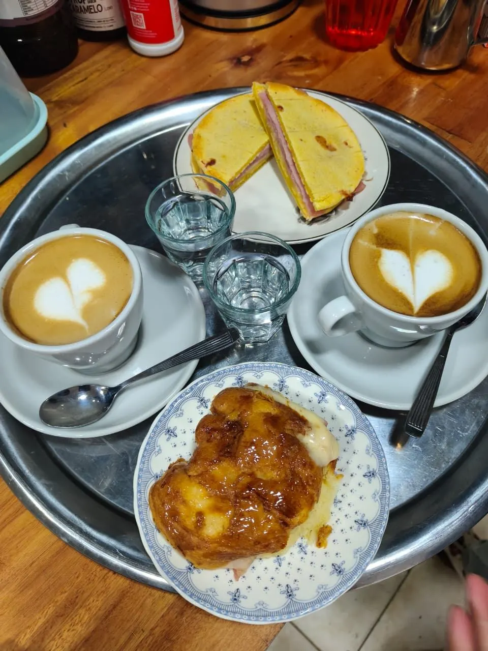 Dos capuchinos con arte latte, tostado de chipá y medialuna rellena